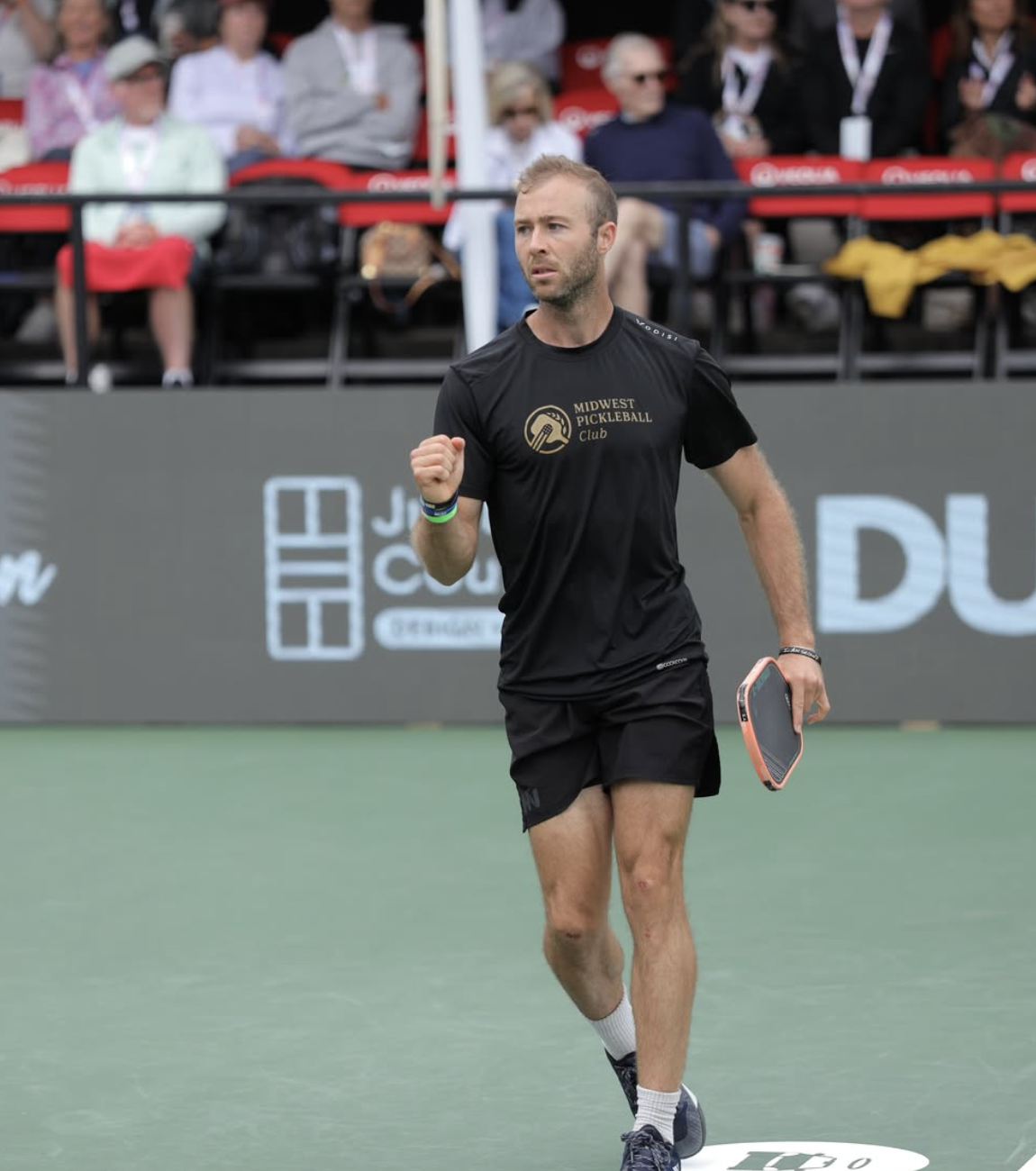 Matthew Barlow celebrates on court during a professional pickleball match while wearing a Midwest Pickleball Club shirt.